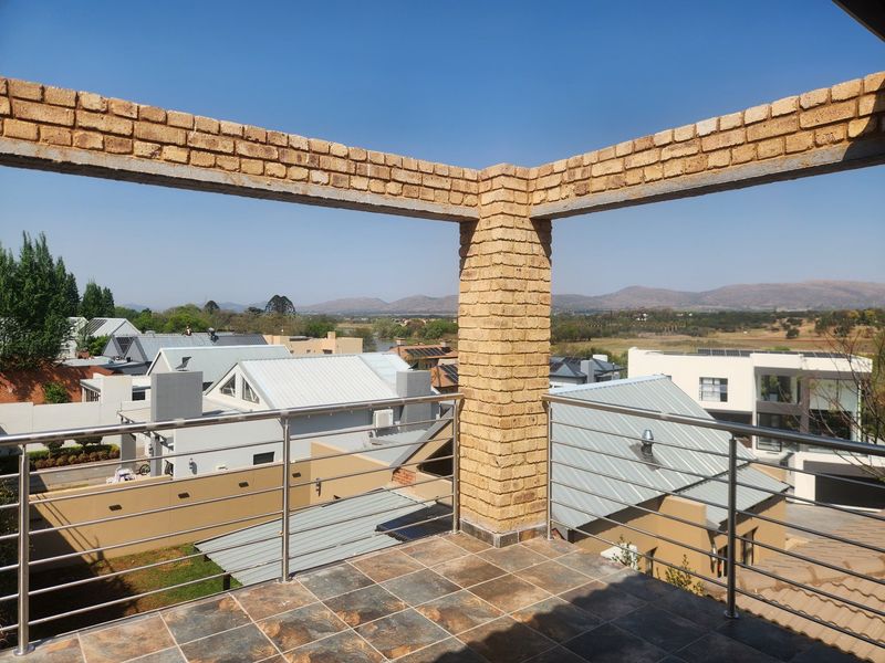 An elevated balcony featuring exposed brick pillars, stainless steel railings, and tiled flooring, offering expansive views of the surrounding neighbourhood and landscape.