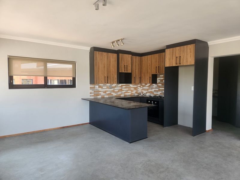 Modern open-plan kitchen featuring two-tone cabinetry, dark countertops, built-in oven, gas hob, and a decorative tiled backsplash.