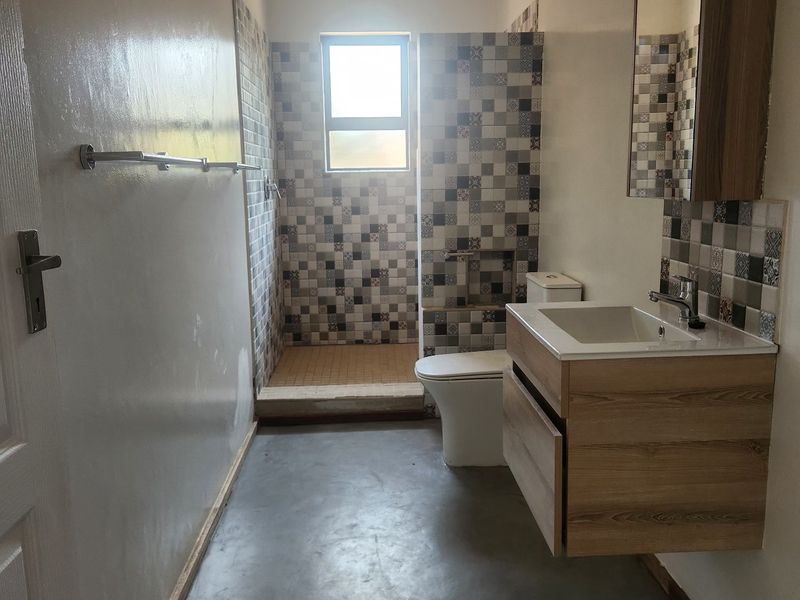 A modern bathroom featuring a wall-mounted vanity, walk-in shower with decorative tiling, and a neutral color palette.