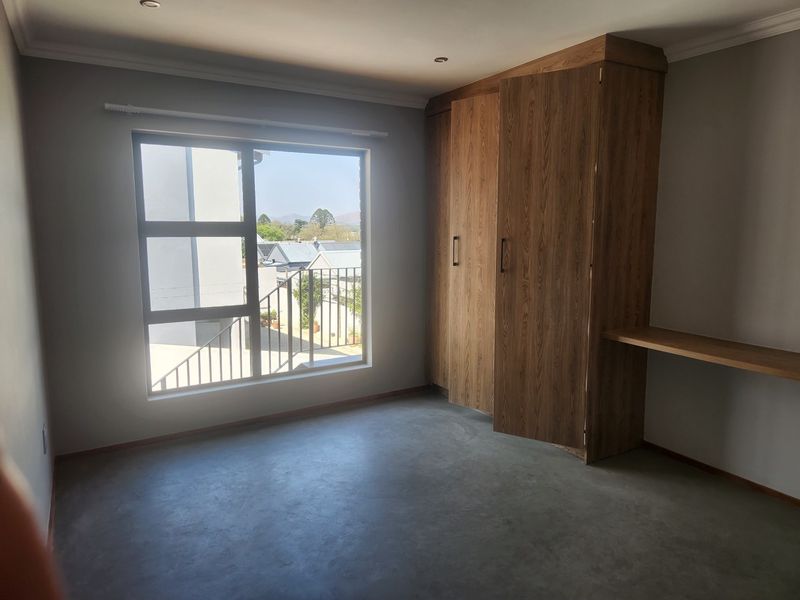 A bright, empty bedroom featuring modern concrete flooring, built-in wooden cupboards, and an integrated desk area with natural light.