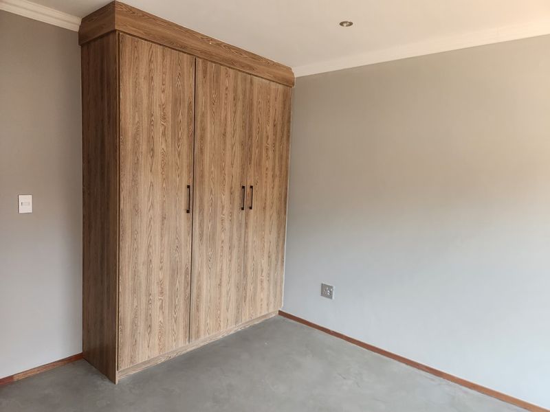 A clean, empty bedroom featuring modern wood-finish built-in cupboards, neutral wall paint, and polished concrete flooring.