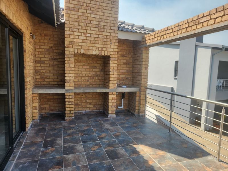 Covered balcony featuring a built-in brick braai, concrete countertop, and integrated prep sink, finished with tiled flooring and a modern stainless steel balustrade.