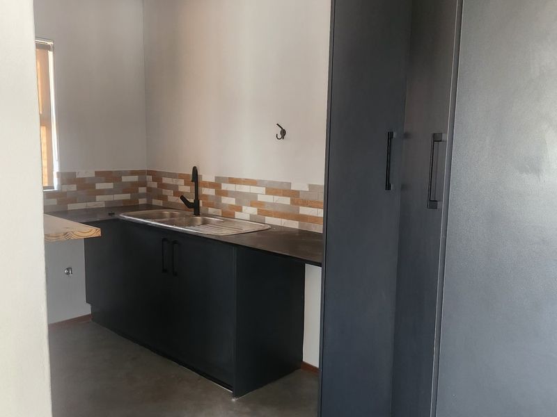 A modern, minimalist scullery featuring dark cabinetry, a stainless steel sink, and a decorative tiled splashback with polished concrete flooring.