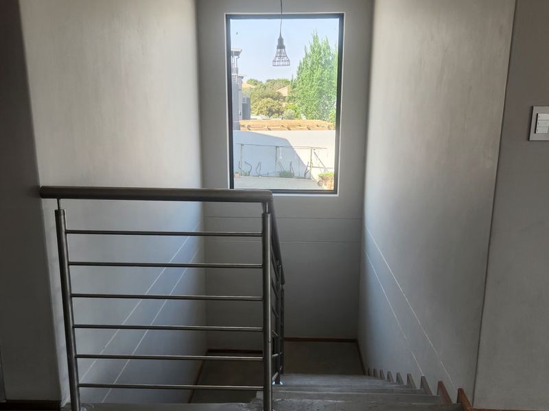A modern staircase featuring a polished concrete finish and a sleek stainless steel balustrade, illuminated by a pendant light and natural window light.