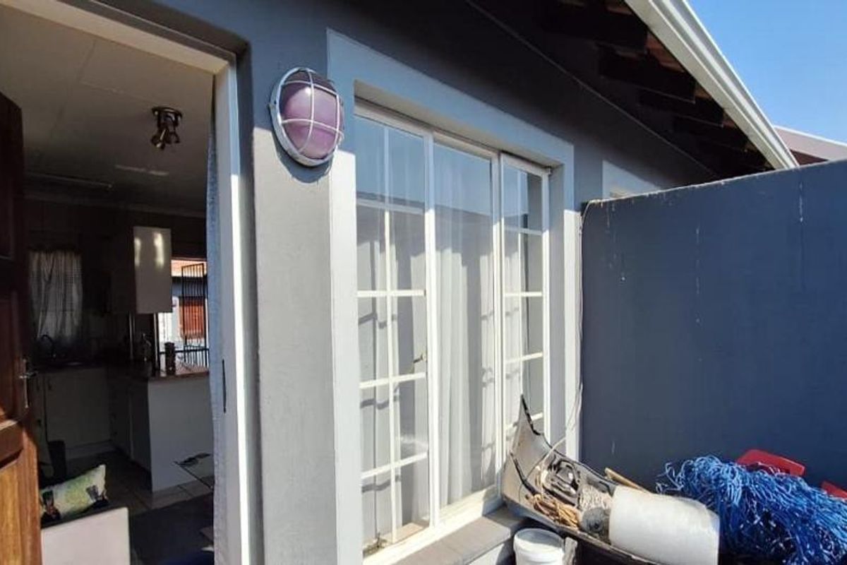 A rear exterior view showing a patio area with a sliding glass door entrance and a timber door leading into the apartment.