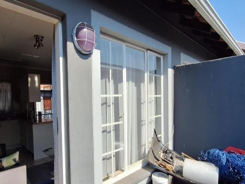 A rear exterior view showing a patio area with a sliding glass door entrance and a timber door leading into the apartment.