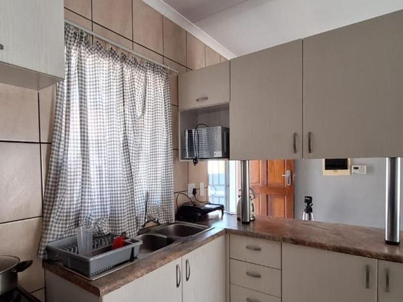 Functional kitchen featuring light-toned cabinetry, laminate countertops, a double basin sink, and a tiled backsplash with a convenient breakfast bar area.