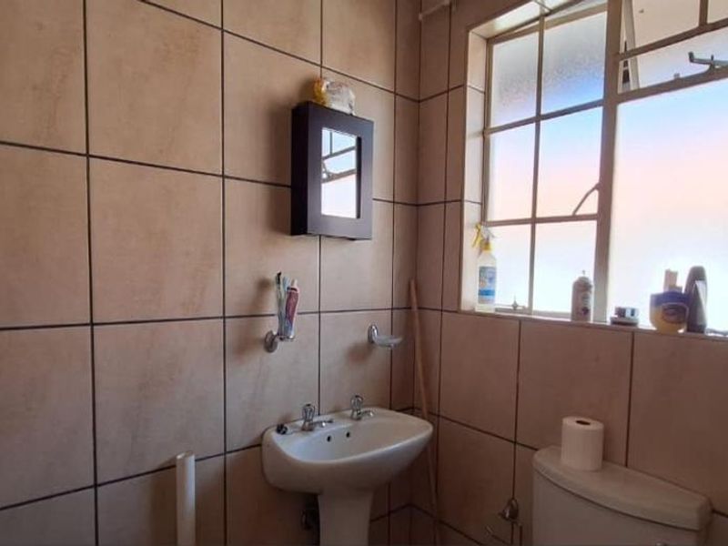 A functional bathroom featuring tiled walls, a pedestal basin, and a toilet, with natural light provided by a window.