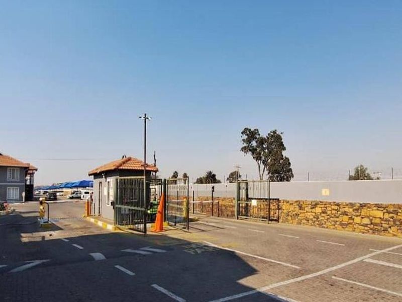 The entrance to the apartment complex features a secure guard house, boom gate access, perimeter walling with electric fencing, and paved visitor parking.