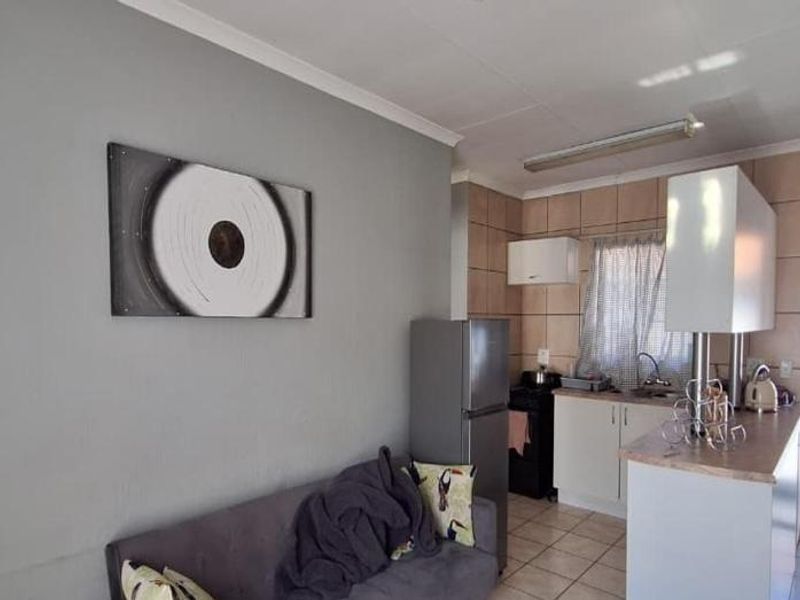 Open-plan living area featuring a compact kitchen with breakfast bar, tiled backsplash, and direct access to an exterior balcony through a security gate.
