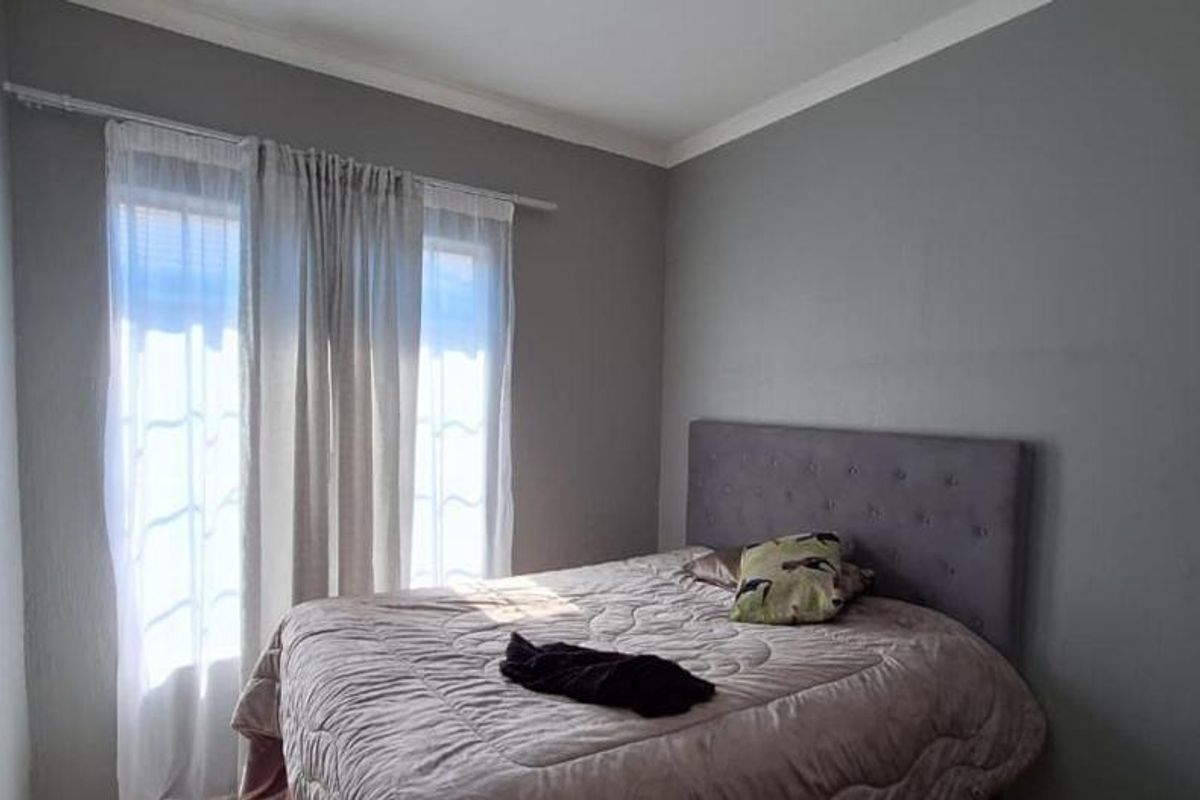 A bedroom featuring neutral grey walls, coving, and a window dressed with a curtain rod and sheer curtains.