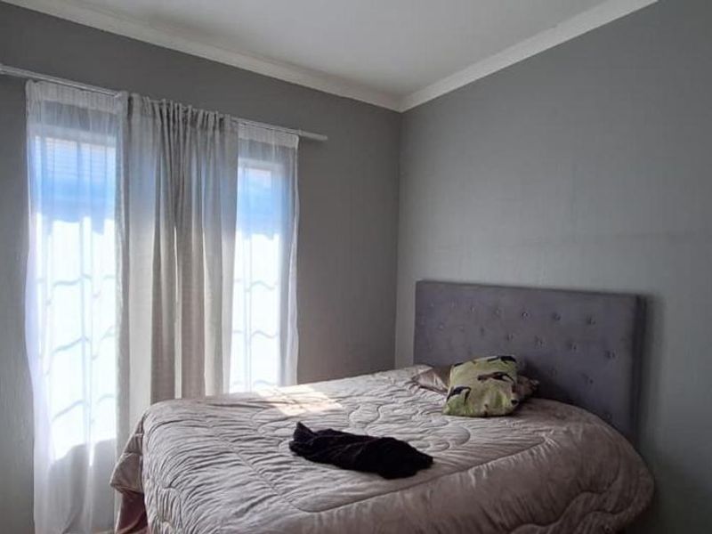 A bedroom featuring neutral grey walls, coving, and a window dressed with a curtain rod and sheer curtains.
