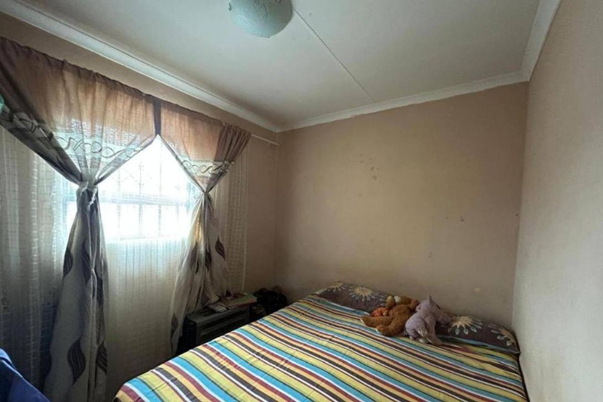 A compact bedroom featuring a window with security bars, coving, and a ceiling light fixture, requiring cosmetic updates to the wall finishes.