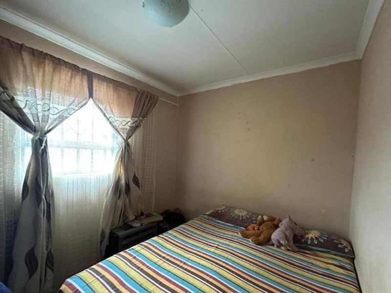 A compact bedroom featuring a window with security bars, coving, and a ceiling light fixture, requiring cosmetic updates to the wall finishes.