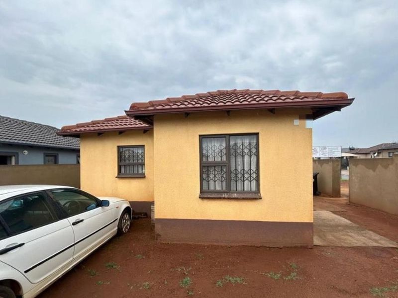 Front view of a single-story residential house featuring a tiled roof, security bars on windows, and a concrete driveway area.