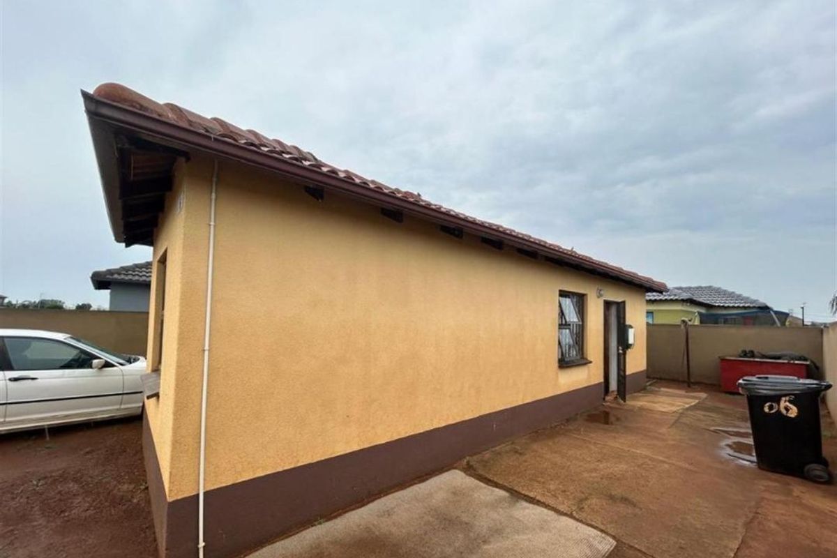 Rear view of the property showing the plastered exterior walls, tiled roof, and paved backyard area.