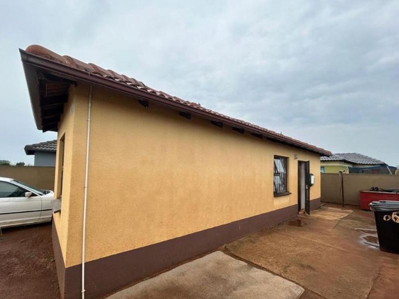 Rear view of the property showing the plastered exterior walls, tiled roof, and paved backyard area.