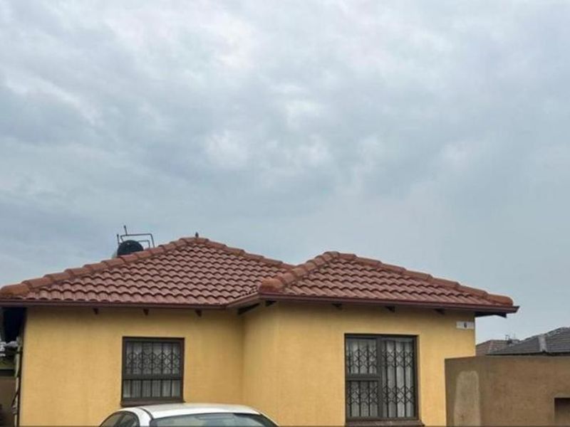 Front elevation of a single-story house featuring a tiled roof, security bars on windows, and a surrounding boundary wall.