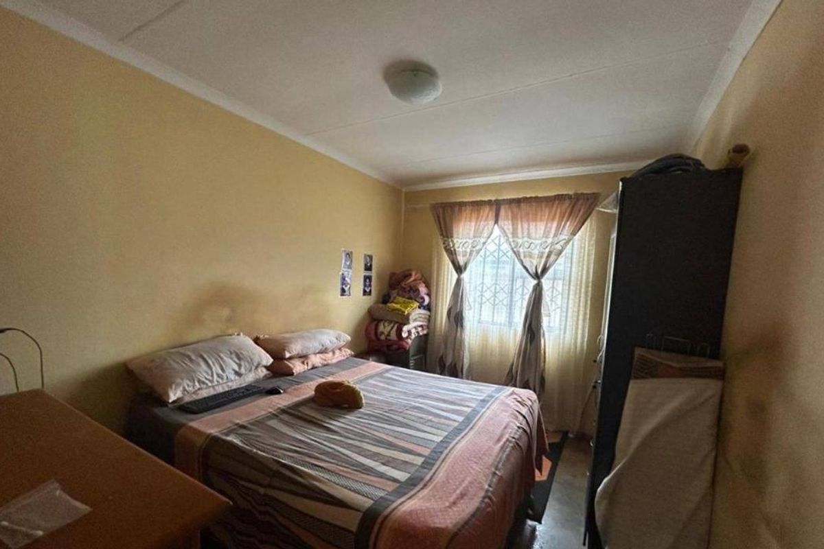 A compact bedroom featuring a window with security bars and standard ceiling finishes, requiring cosmetic updates to improve the overall aesthetic.
