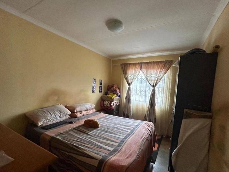 A compact bedroom featuring a window with security bars and standard ceiling finishes, requiring cosmetic updates to improve the overall aesthetic.