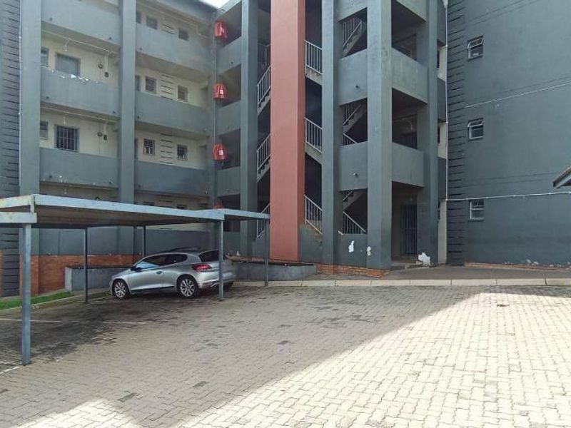 Exterior view of an apartment complex featuring a paved parking area with carports and a multi-story building with external stairwell access.