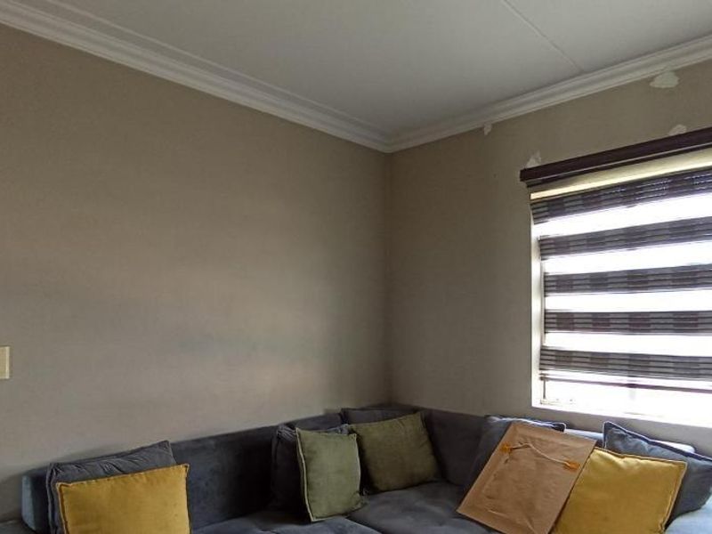 A living room area featuring crown molding and modern zebra blinds, showing some minor wear on the wall surfaces near the ceiling.