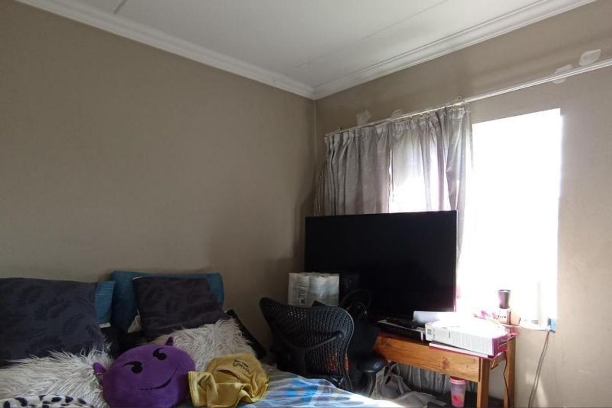 A bedroom featuring a window with a curtain rod and crown molding, showing signs of wear on the ceiling and walls.