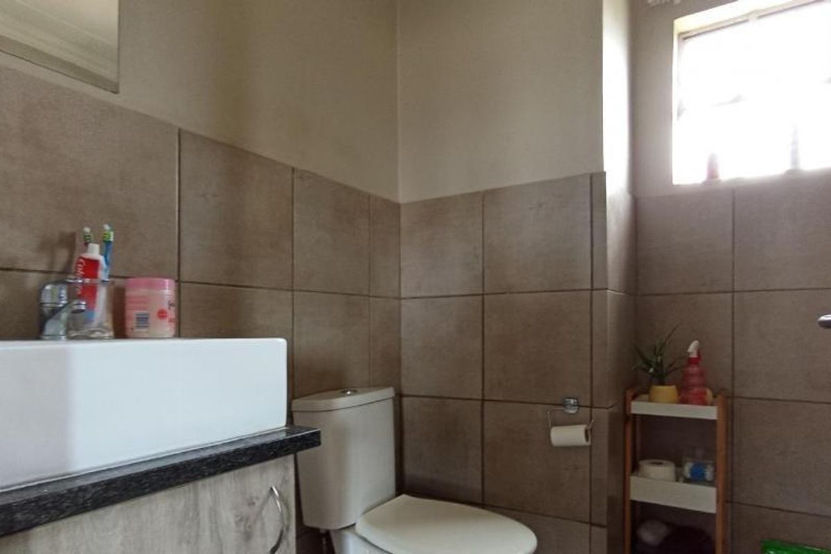 A functional bathroom featuring a modern basin with vanity cabinet, toilet, and neutral wall tiling.