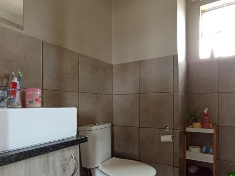 A functional bathroom featuring a modern basin with vanity cabinet, toilet, and neutral wall tiling.
