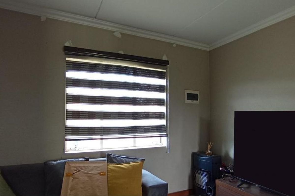 A living room featuring a window with roller blinds and visible wall surface imperfections requiring maintenance or repainting.