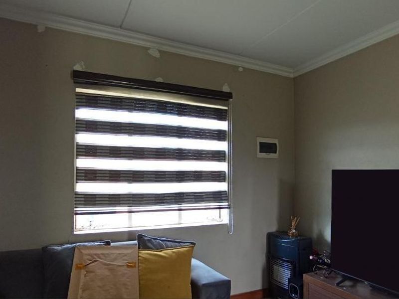 A living room featuring a window with roller blinds and visible wall surface imperfections requiring maintenance or repainting.