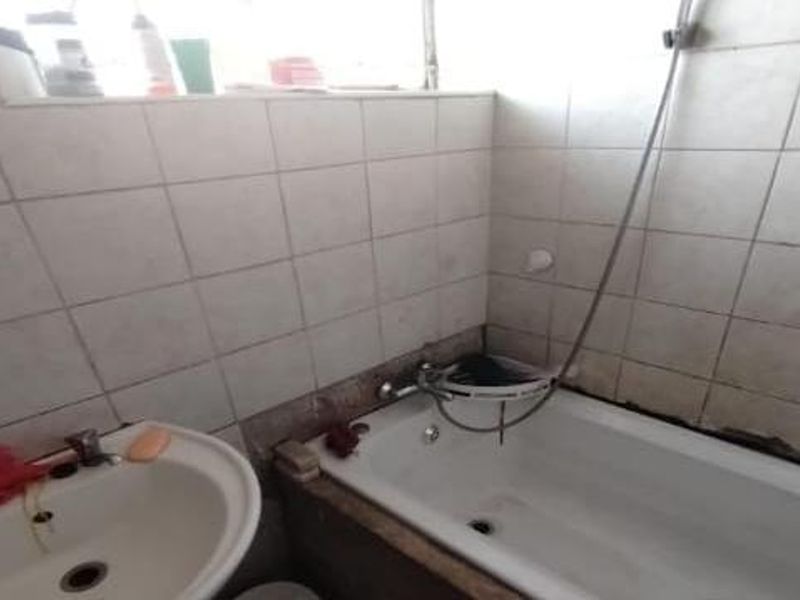A dated bathroom featuring a standard bathtub with shower mixer and a pedestal basin, requiring maintenance to tile grout and sealant.