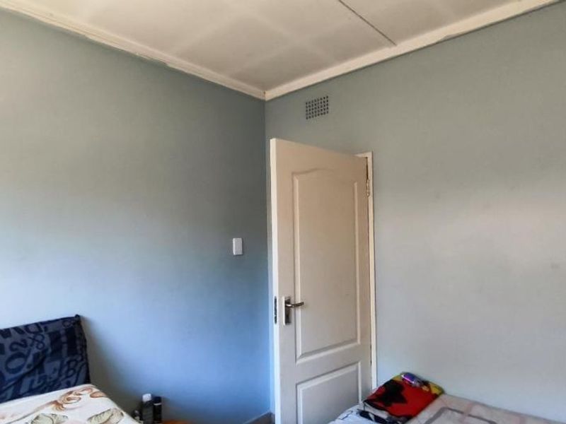 A bedroom featuring a standard internal door and ceiling ventilation, showing signs of wear on the ceiling panels.
