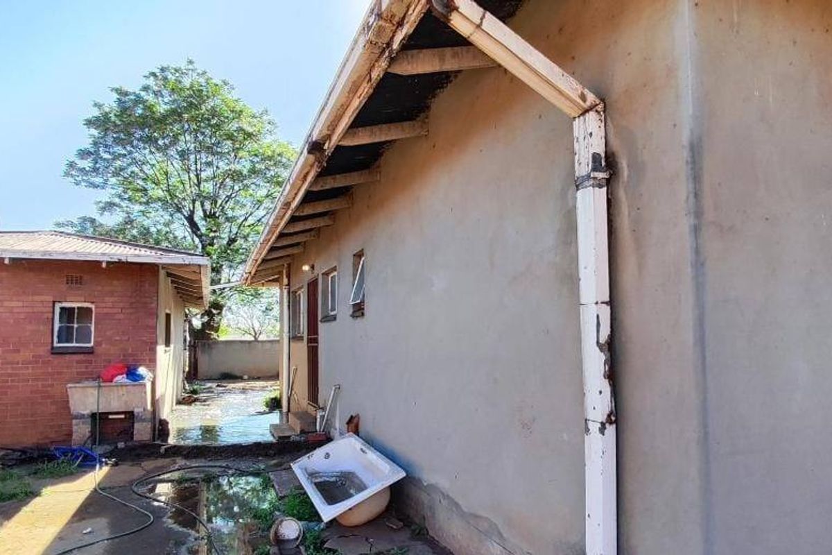 Rear exterior view of the property showing a brick outbuilding, exposed roof rafters, and signs of water accumulation and exterior maintenance requirements.