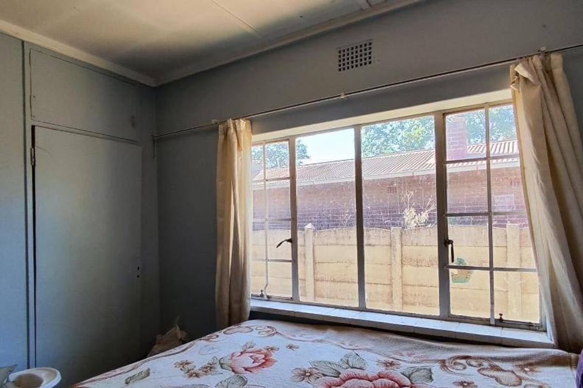 A bedroom featuring a built-in cupboard and a large steel-framed window, offering a functional space with potential for cosmetic updates.