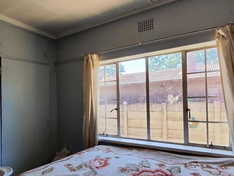 A bedroom featuring a built-in cupboard and a large steel-framed window, offering a functional space with potential for cosmetic updates.