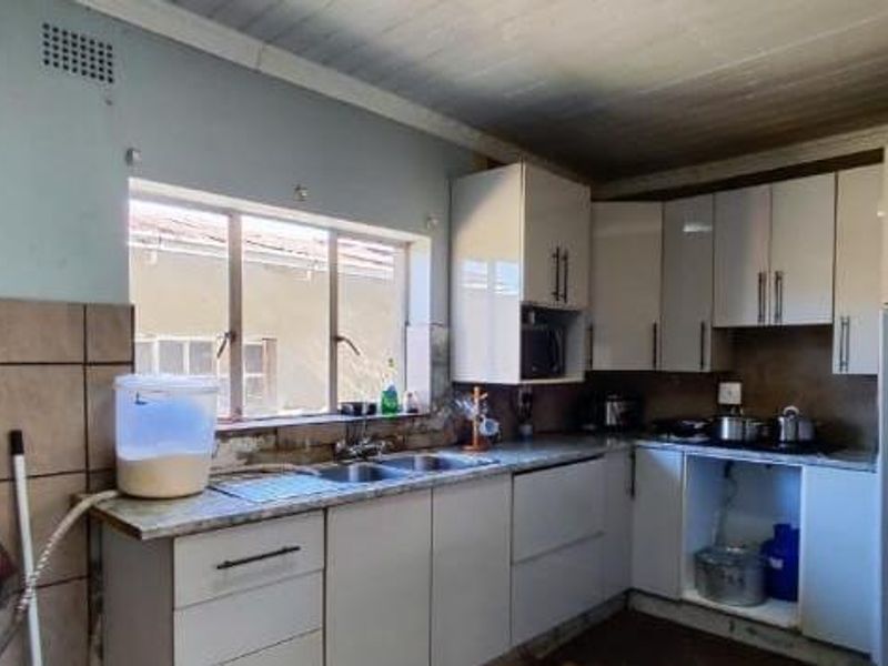 A functional kitchen featuring built-in cabinetry, a double basin sink, and tiled splashbacks, offering potential for cosmetic updates and modernization.