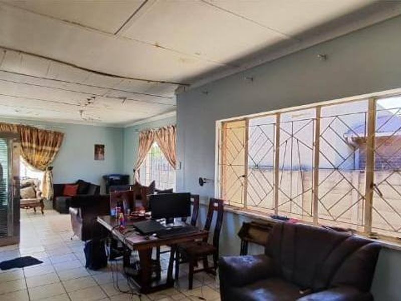 Spacious living area featuring tiled flooring and security bars on windows, requiring ceiling repairs and cosmetic updates to improve the overall condition.