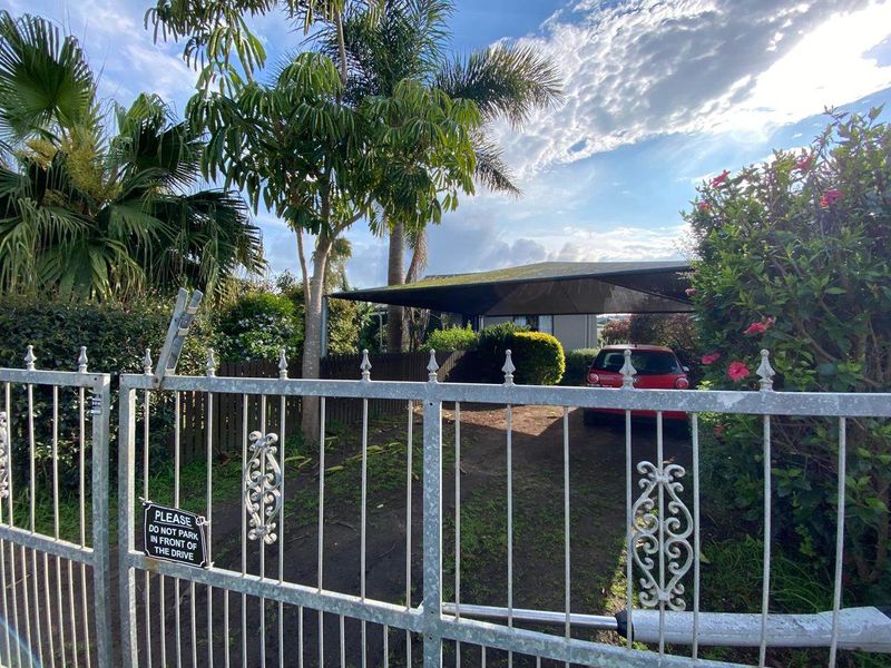Front view of the property featuring a metal security gate, a driveway, and a carport with a mature garden.