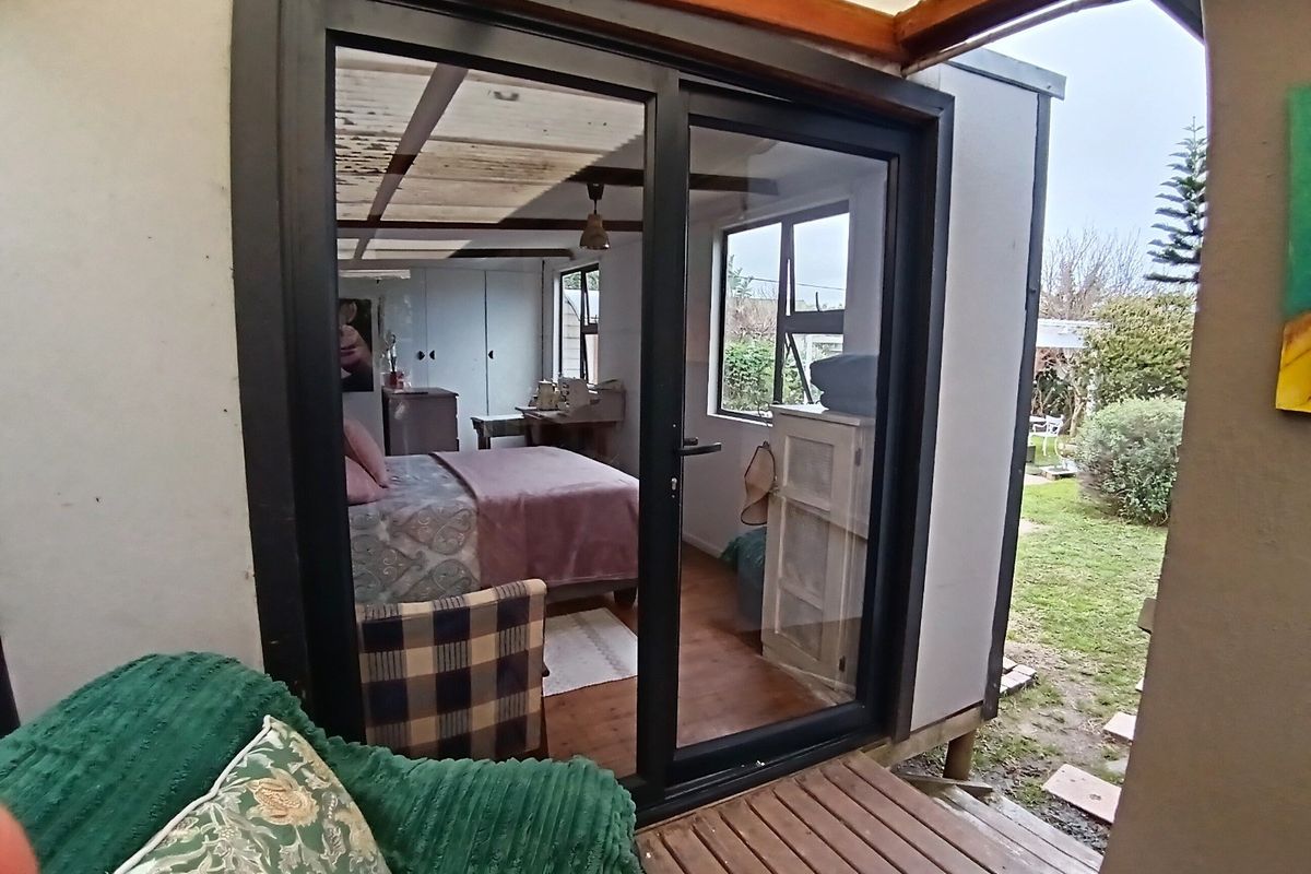 A bedroom featuring timber flooring and built-in cupboards, with direct access to an outdoor timber deck through a modern sliding glass door.