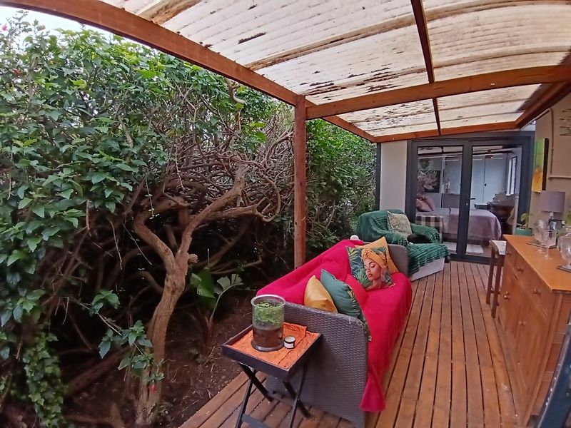 A covered outdoor patio featuring timber decking and a translucent roof, providing a sheltered transition space between the garden and the interior living area.