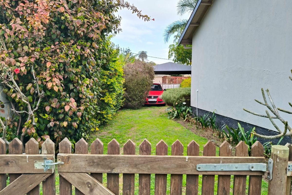 A view of the rear garden area featuring a wooden picket gate, established landscaping, and a lawn leading towards the side of the house.