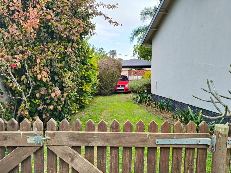 A view of the rear garden area featuring a wooden picket gate, established landscaping, and a lawn leading towards the side of the house.