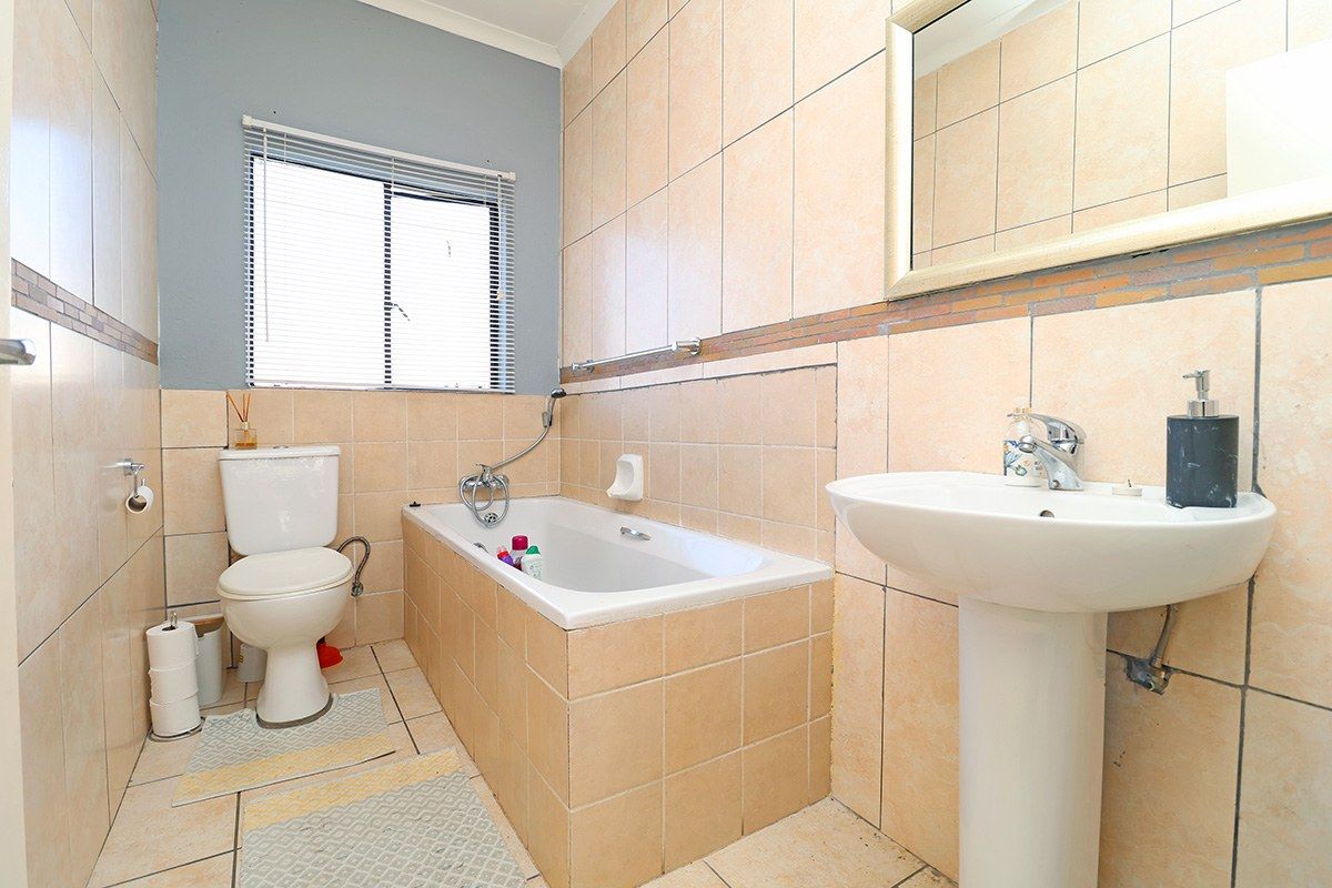 A functional bathroom featuring a pedestal basin, built-in bathtub, and toilet, finished with neutral wall and floor tiling.