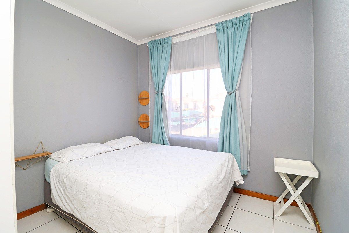 A functional bedroom featuring tiled flooring, neutral grey walls, and a window with curtains.