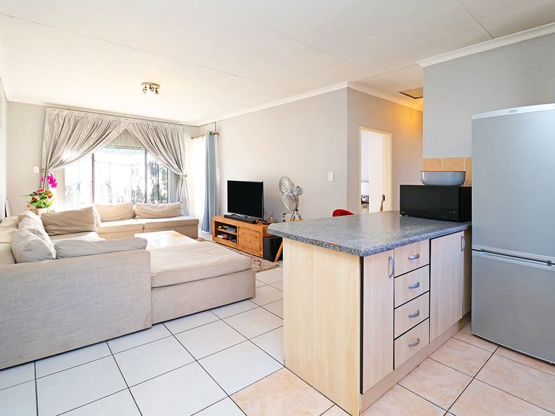 Open-plan living area featuring tiled flooring and a functional kitchen island with laminate cabinetry, seamlessly connecting the kitchen and lounge space.