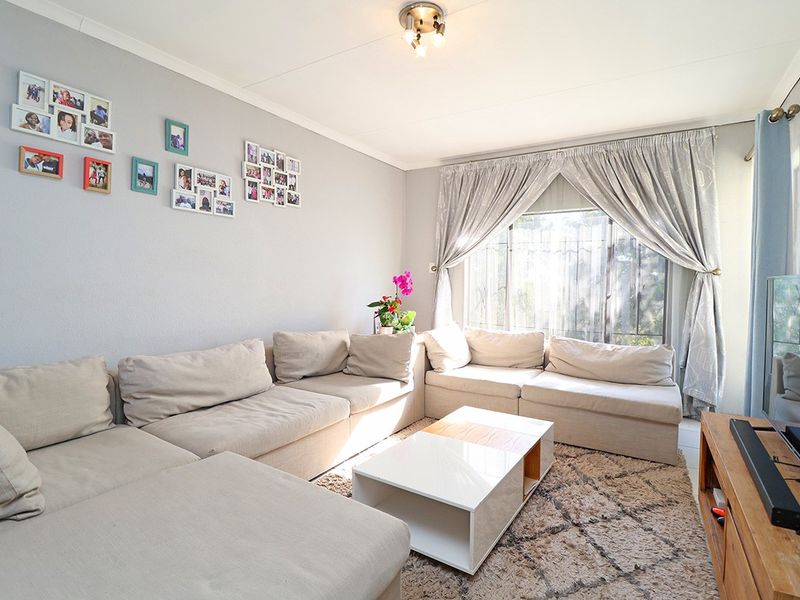 A comfortable living room featuring neutral walls, a large window with security bars, and overhead lighting, providing a functional and well-lit space.