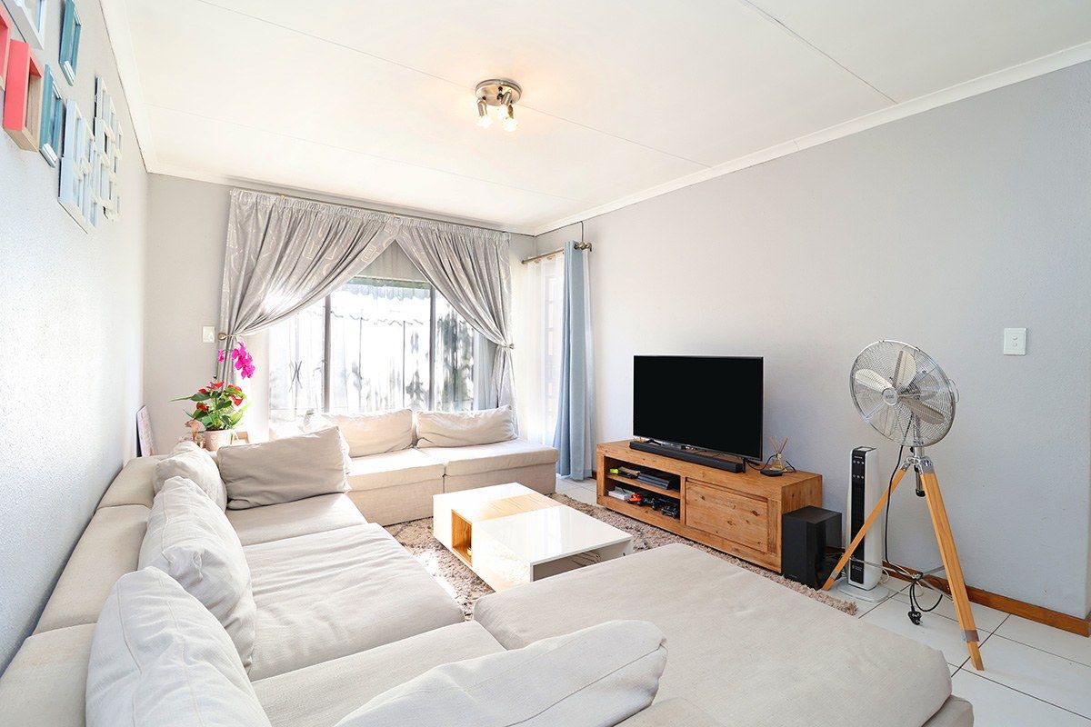 A bright and comfortable living room featuring tiled flooring and large windows with curtain rails, providing a functional and inviting space.