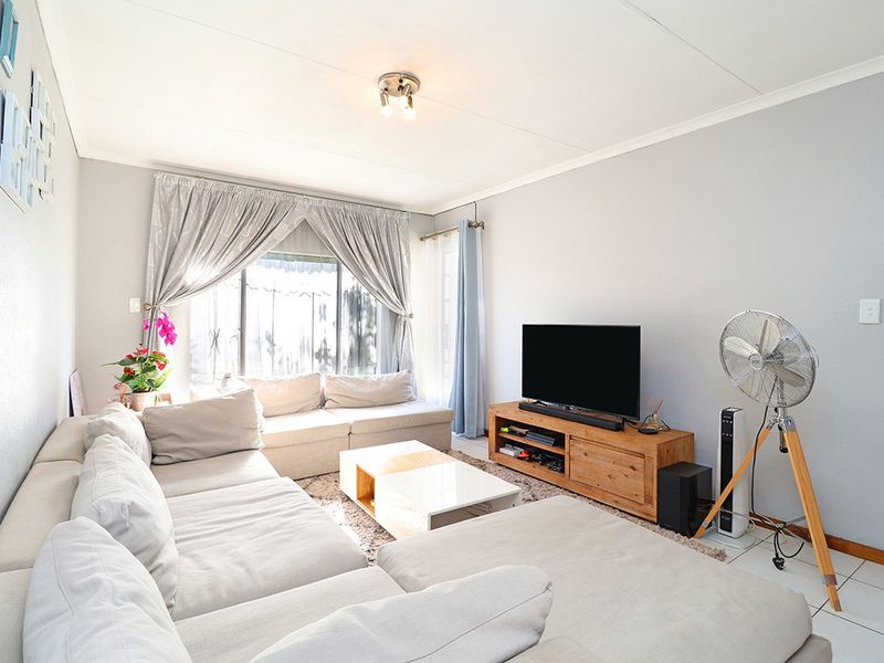 A bright and comfortable living room featuring tiled flooring and large windows with curtain rails, providing a functional and inviting space.