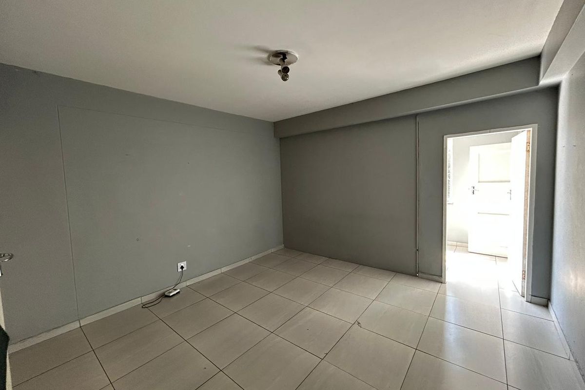 An empty bedroom featuring neutral grey walls and light-colored floor tiles, providing a blank canvas for personalization.